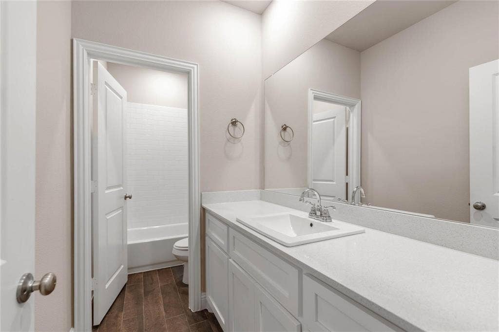 1253 Carinna Drive, Anna, TX 75409 Bathroom featuring a single-sink vanity with a quartz countertop, white shaker-style cabinetry, a large wall-mounted mirror, and wood-finish flooring
