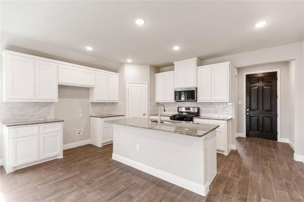 1253 Carinna Drive, Anna, TX 75409 Kitchen featuring white shaker-style cabinetry, stone countertops, a center island with a stainless steel sink, wood-finish flooring, and a tiled backsplash