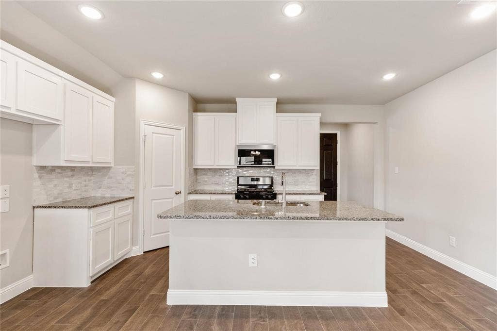 1253 Carinna Drive, Anna, TX 75409 Kitchen featuring white shaker-style cabinetry, stone-surface countertops, a tiled backsplash, wood-finish flooring, and a central island with an integrated stainless steel sink