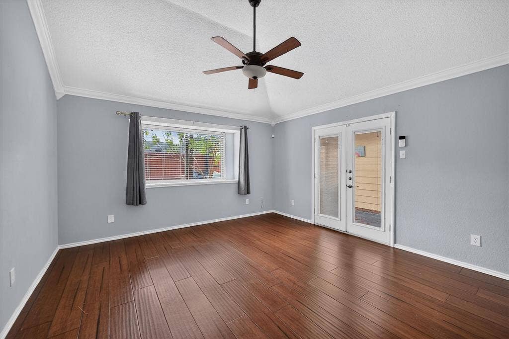 Vaulted ceiling with a central paddle fan, wood-finish flooring, crown molding, and glass-paneled double doors
