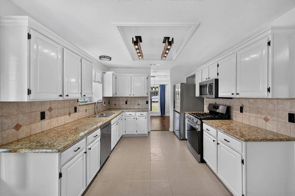 Kitchen featuring white shaker-style cabinetry, stone-surface countertops, tile backsplash, stainless steel appliances, and tile flooring