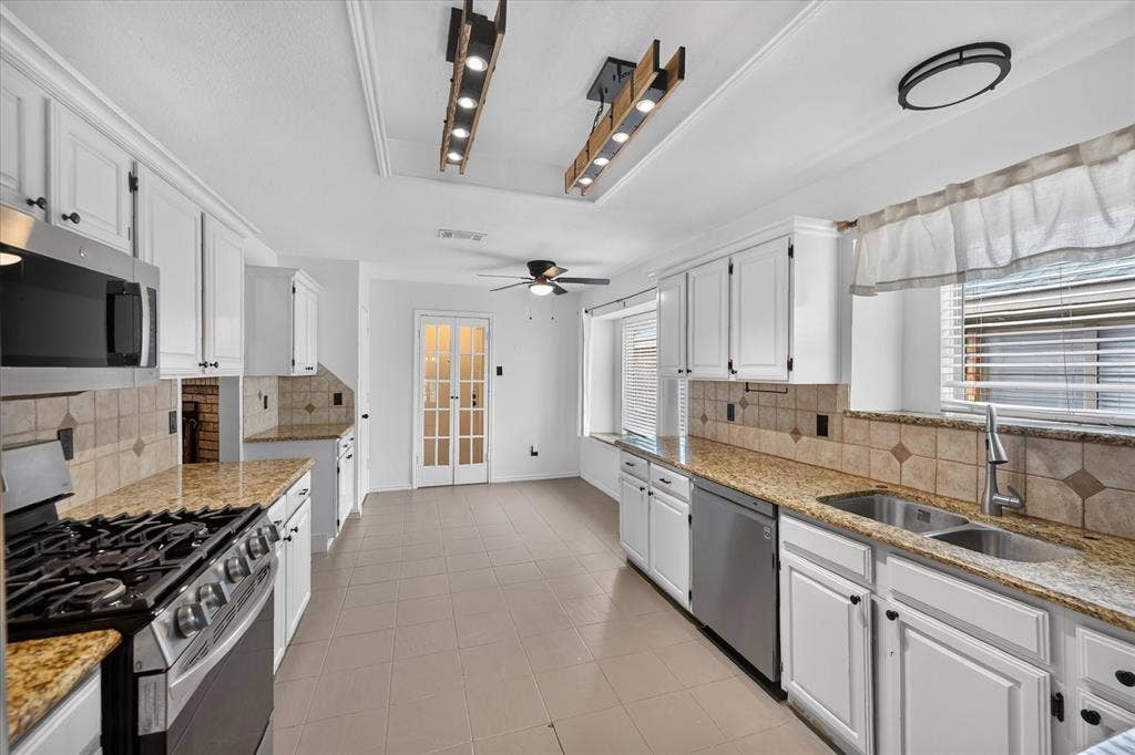 Kitchen featuring white cabinetry, stone countertops, stainless steel appliances, ceramic tile backsplash, and dual wood-frame linear light fixtures
