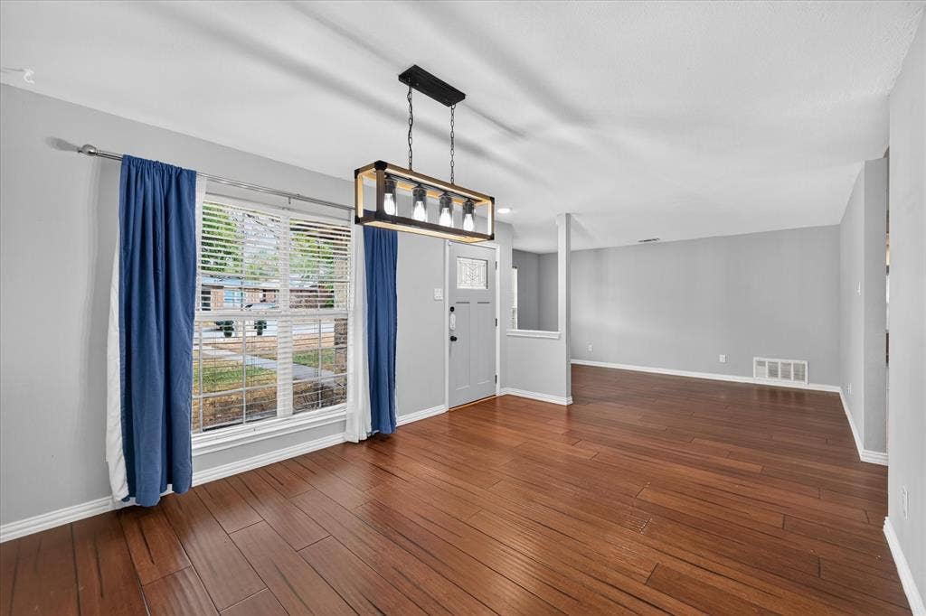Wood-finish flooring, rectangular multi-light pendant fixture, and single-panel door with glass inset