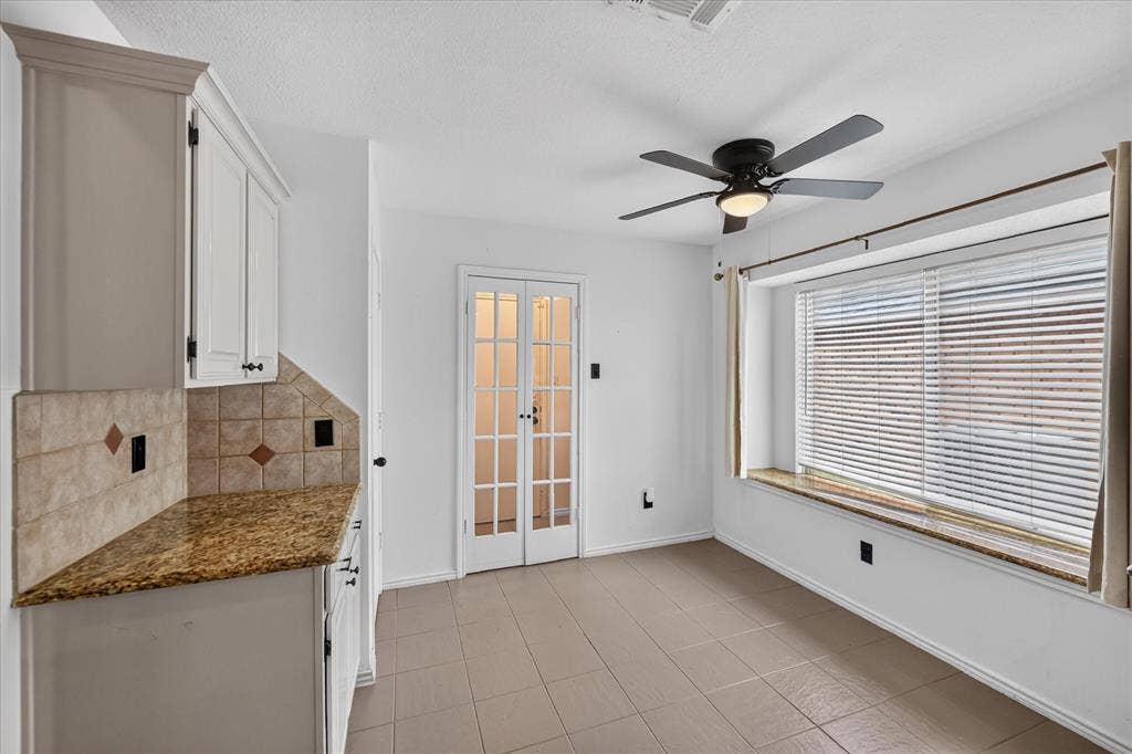 White cabinetry, stone-finish countertops, tile backsplash, built-in window seat, and multi-pane French doors