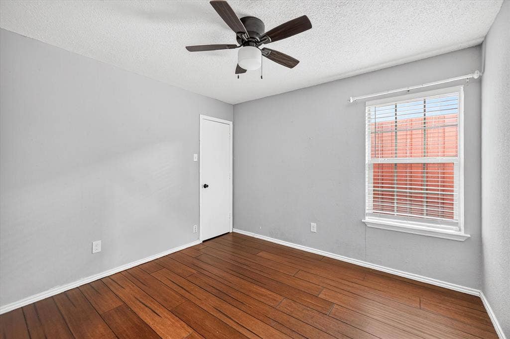 Room featuring wood-finish flooring, a ceiling fan with integrated light fixture, and a window with horizontal blinds