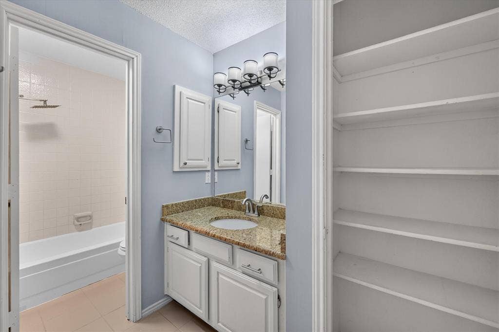 Bathroom featuring a stone-surface vanity with an integrated undermount sink, multi-light fixture, built-in shelving unit, and a tiled tub-shower combination