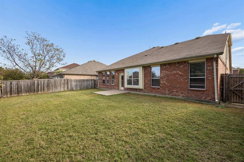 861 Crockett Drive, Lavon, TX 75166 The home's rear exterior showcases classic red brick construction accented by light-colored trim and multiple windows. A fully fenced backyard offers a private outdoor setting with an open lawn and a concrete patio just off the back of the home. With room to enjoy outdoor activities, gardening, or casual gatherings, this backyard offers a wonderful opportunity to create a personalized outdoor retreat.