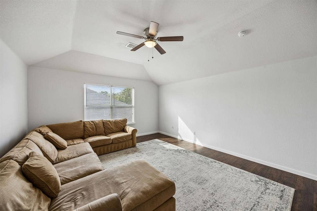 861 Crockett Drive, Lavon, TX 75166 A spacious upstairs living area featuring a vaulted ceiling, ceiling fan, and rich wood-look flooring that extends throughout the room. Neutral wall colors and a large window invite natural light inside, creating a bright, open atmosphere. The generous floor space offers flexibility for a secondary living area, game room, media room, or comfortable retreat.