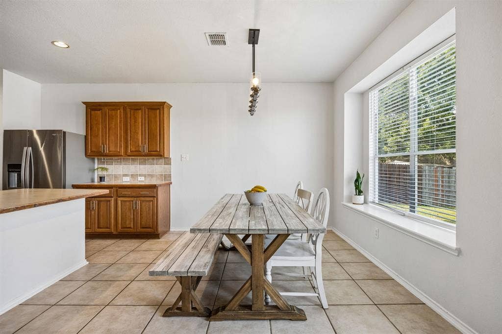 861 Crockett Drive, Lavon, TX 75166 The dining area is filled with natural light from a generously sized window overlooking the backyard, creating a bright and cheerful setting for everyday meals and special gatherings. Neutral tile flooring offers durability and easy maintenance, while the adjoining kitchen provides convenient access to the main living spaces. A contemporary pendant light adds a refined finishing touch to this welcoming dining nook.