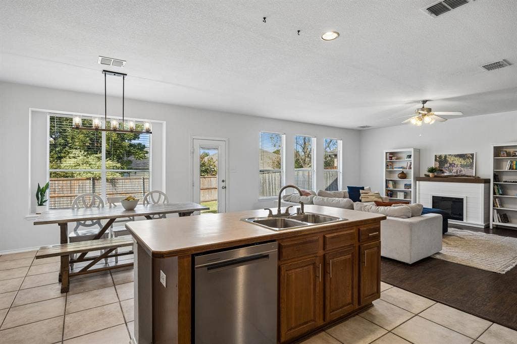 861 Crockett Drive, Lavon, TX 75166 Enjoy the versatility of this open-concept kitchen and dining area, designed to bring functionality and connection together. The kitchen features abundant wood cabinetry, expansive counter space, a built-in dishwasher, and a convenient center island with an integrated sink. Natural light pours through multiple windows, illuminating the dining area and adjoining living room. Tile flooring in the kitchen and dining space transitions beautifully to wood-look flooring in the living area, creating distinct yet connected spaces.