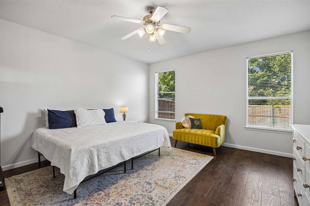 861 Crockett Drive, Lavon, TX 75166 This spacious primary bedroom offers a comfortable retreat with neutral walls, warm wood-look flooring, and ample natural light streaming through two windows. A ceiling fan with integrated lighting adds everyday comfort, while the generous floor space allows for a variety of room arrangements. The light, neutral palette creates a welcoming atmosphere with plenty of potential to personalize the space.