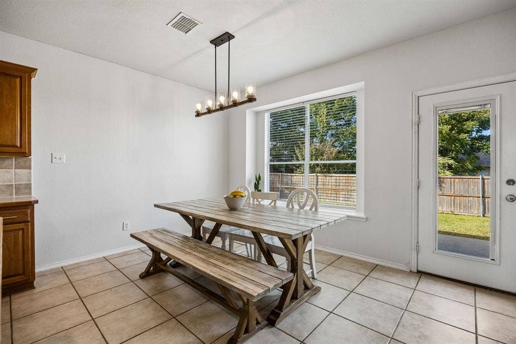 861 Crockett Drive, Lavon, TX 75166 Bright and inviting, the dining area features a large window with backyard views and a glass-paneled exterior door that provides convenient access to the outdoor space. Neutral tile flooring extends throughout the area, offering both practicality and a cohesive look. A modern linear chandelier adds character overhead, while the open connection to the kitchen makes serving meals and entertaining guests a breeze.