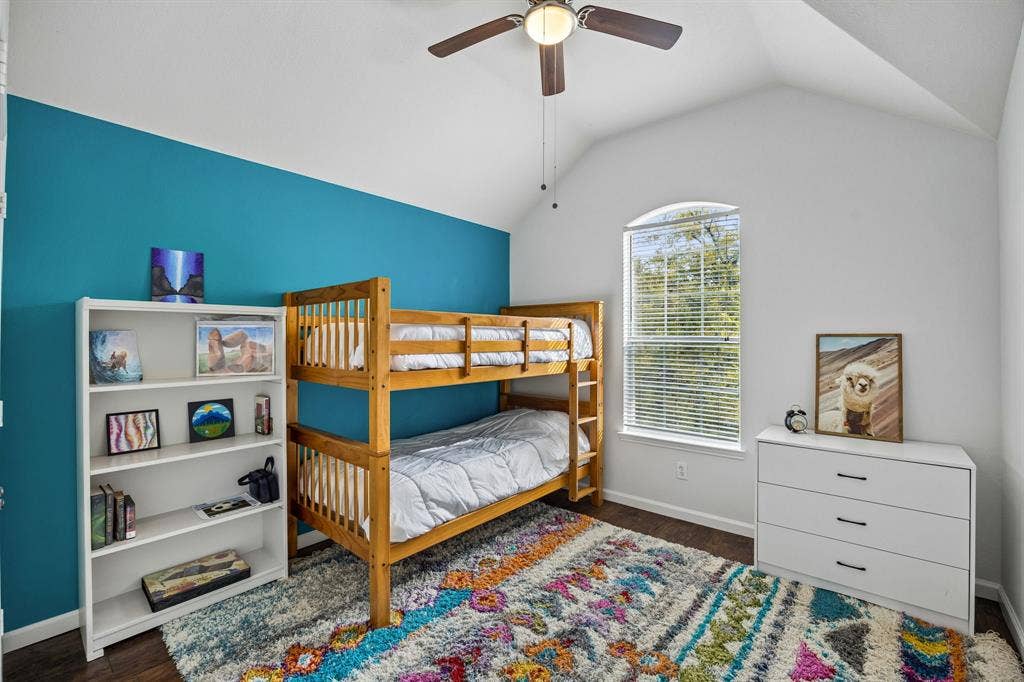 861 Crockett Drive, Lavon, TX 75166 Enjoy the character and charm of this bedroom, featuring a vaulted ceiling, bold turquoise accent wall, and a beautiful arched-top window that allows natural light to filter inside. Rich wood-look flooring and crisp white trim complement the colorful walls, while the spacious layout provides flexibility for a variety of bedroom arrangements and personal touches.