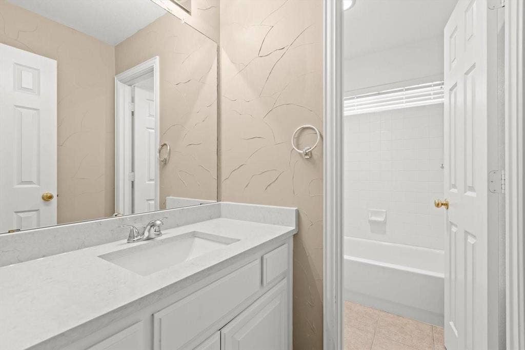 4120 Silverthorne Street, Richardson, TX 75082 White vanity with stone-style countertop and integrated sink, large wall-mounted mirror, and tile-surround shower and tub combination
