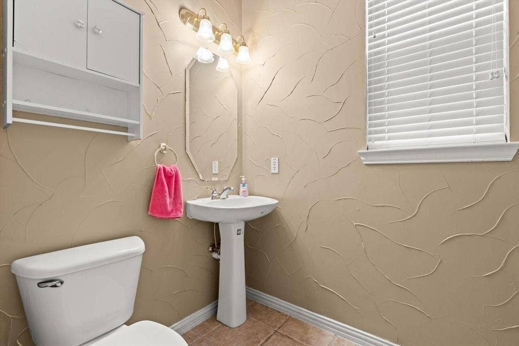 4120 Silverthorne Street, Richardson, TX 75082 Pedestal sink, wall-mounted storage cabinetry, octagonal vanity mirror, multi-light fixture, and textured wall finish