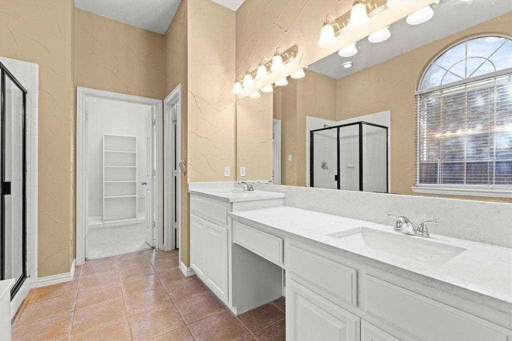 4120 Silverthorne Street, Richardson, TX 75082 Bathroom featuring a dual-sink vanity with a solid-surface countertop, an arched window, tile flooring, and a glass-enclosed shower