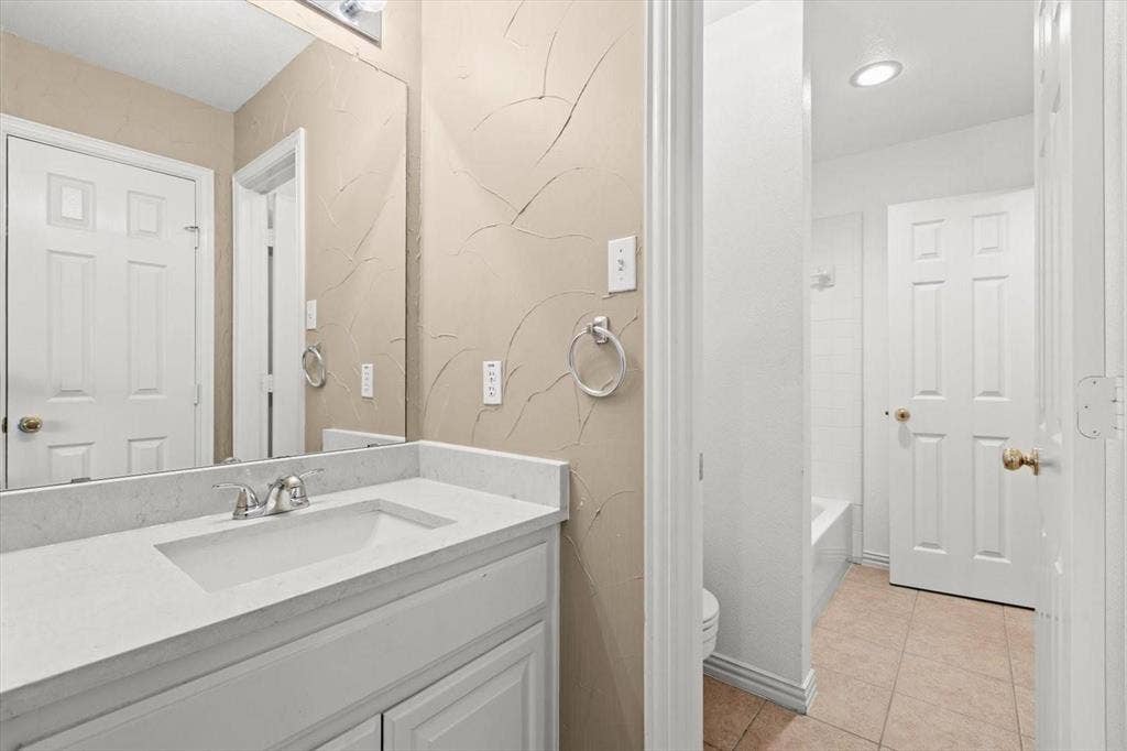 4120 Silverthorne Street, Richardson, TX 75082 Bathroom vanity featuring white cabinetry, a light-toned solid surface countertop, an integrated rectangular basin, and a wall-to-wall mirror with textured wall finish