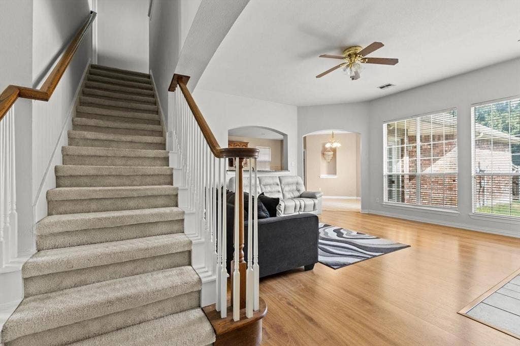 4120 Silverthorne Street, Richardson, TX 75082 Staircase featuring carpeted steps, a wood-finish handrail, and white balusters, wooden-finish flooring, large windows, and a ceiling-mounted light fixture with a fan