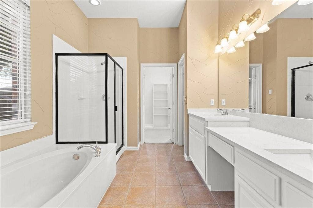 4120 Silverthorne Street, Richardson, TX 75082 Bathroom featuring a dual-sink vanity with white cabinetry and solid-surface countertops, an oval soaking tub, a separate glass-enclosed shower, and tile flooring