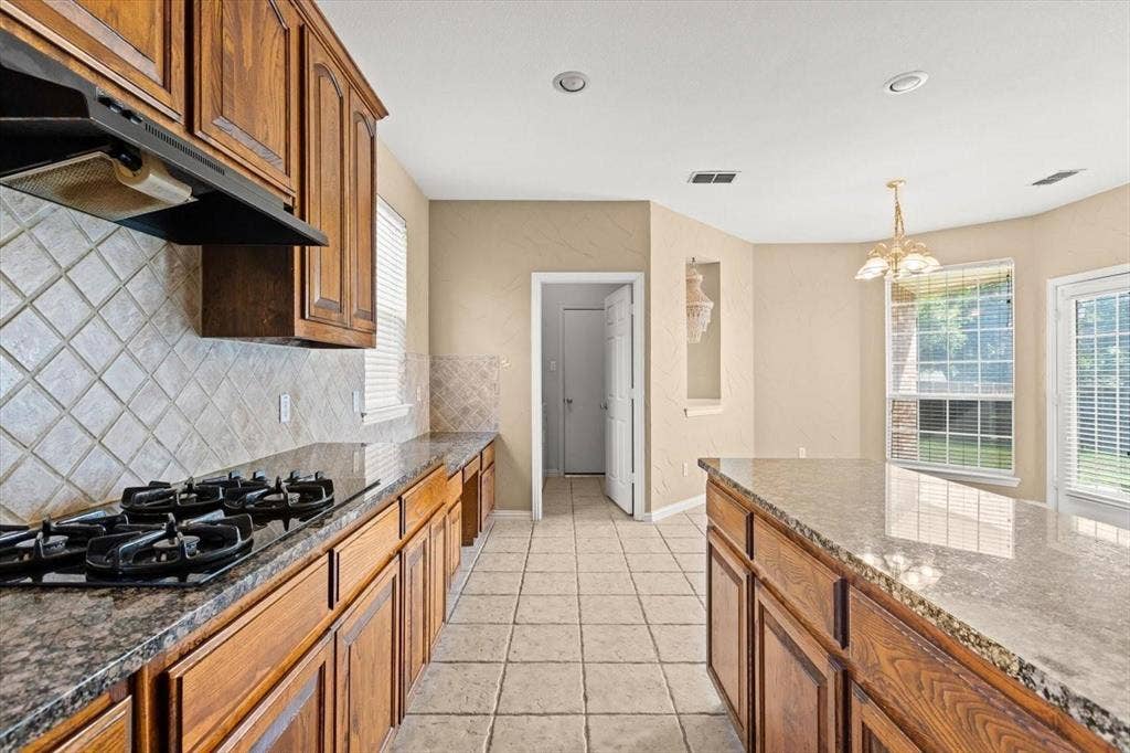 4120 Silverthorne Street, Richardson, TX 75082 Kitchen featuring stained wood cabinetry, stone-finish countertops, diagonal tile backsplash, center island, and tile flooring