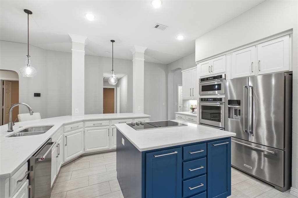 4010 Azure Lane, Addison, TX 75001 A chef-inspired kitchen with crisp white cabinetry, bright counters, glass pendant lights and a built-in wall oven and microwave. The deep navy island steals the show.