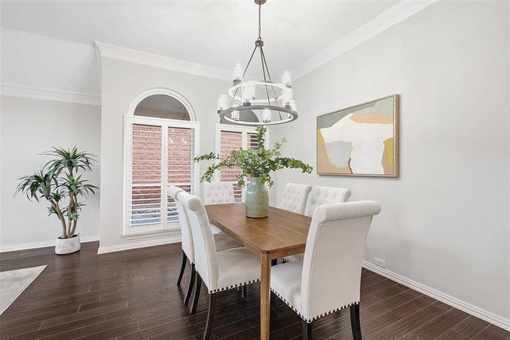 4010 Azure Lane, Addison, TX 75001 A formal dining room made for hosting, with a statement chandelier, plantation shutters on arched windows, and rich dark wood floors.