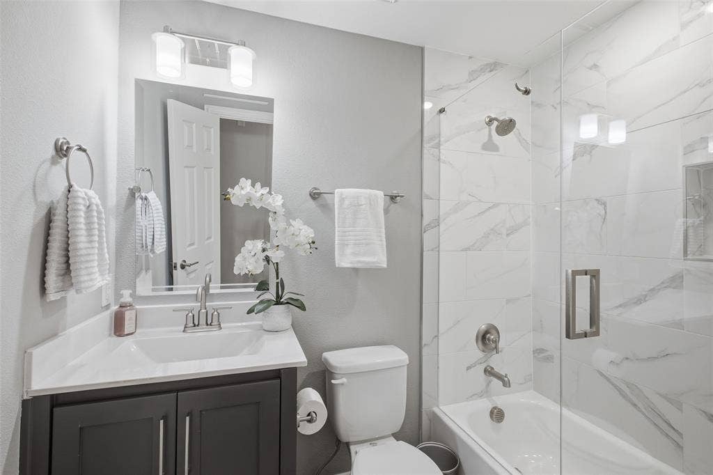 4010 Azure Lane, Addison, TX 75001 The updated guest bath is crisp and modern, with marble-look tile, a frameless glass enclosure and contemporary fixtures.