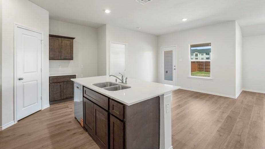 708 Rock Point Road, Josephine, TX 75135 Kitchen island with integrated double basin sink, white countertops, dark wood-finish cabinetry, and wood-finish flooring