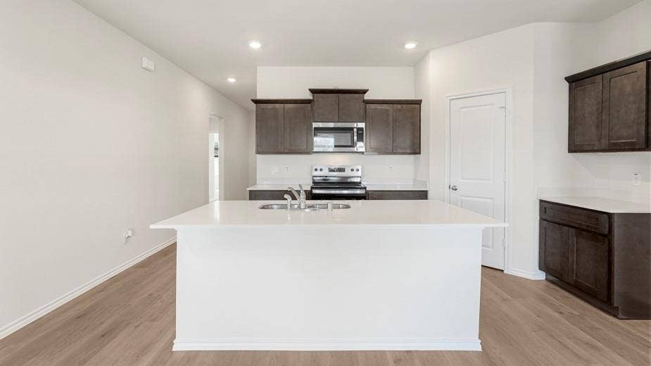 708 Rock Point Road, Josephine, TX 75135 Kitchen featuring a large island with sink, stainless steel appliances, dark wood-finish cabinetry, light countertops, and wood-finish flooring