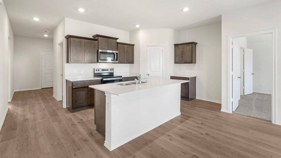 708 Rock Point Road, Josephine, TX 75135 Kitchen featuring an island with a built-in sink, wood-finish flooring, recessed lighting, white countertops, and dark wood cabinetry