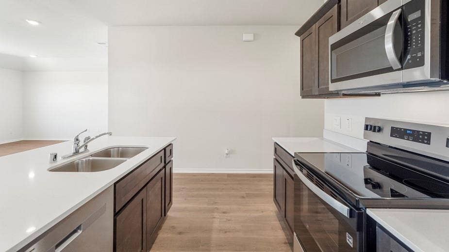 708 Rock Point Road, Josephine, TX 75135 Kitchen featuring an island with a double basin sink, dark wood-finish cabinetry, light-toned countertops, a stainless steel microwave, and a black range