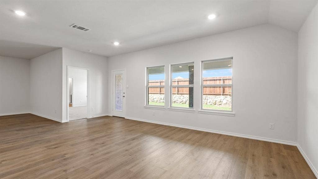 Spacious room featuring wood-finish flooring, white walls, and a vaulted ceiling