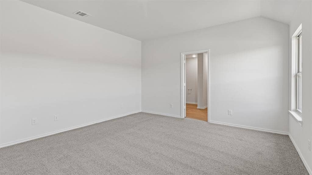 Spacious room featuring vaulted ceilings, light gray carpeting, and a window for natural illumination