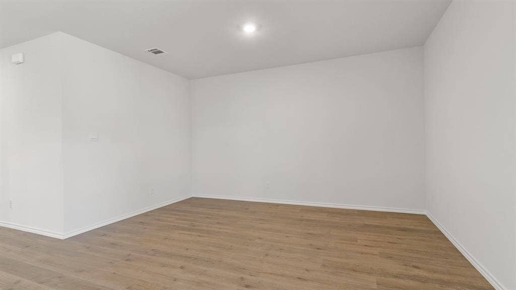 Spacious room featuring light wood-finish flooring, white baseboards, bright white walls, and recessed lighting