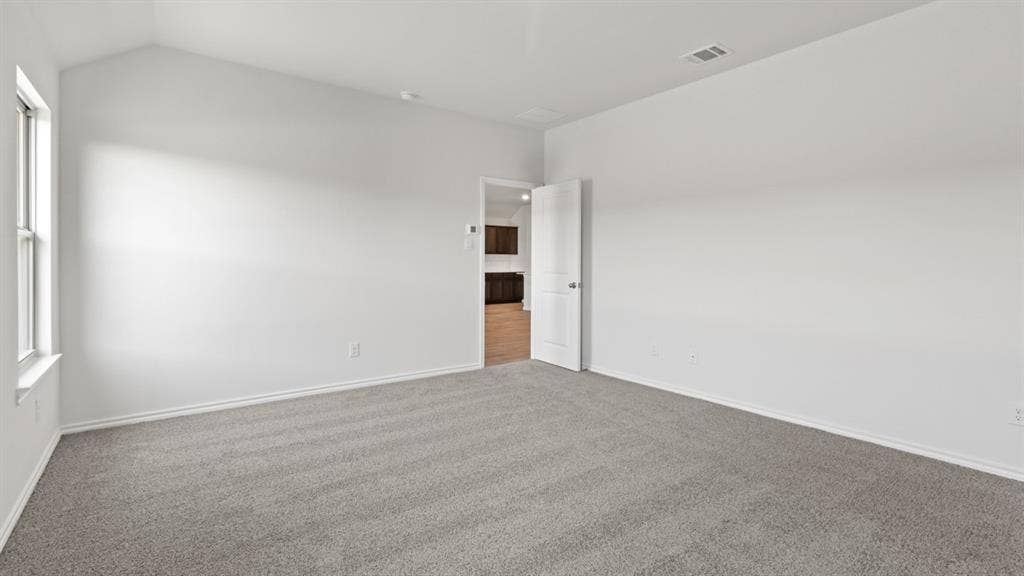 Spacious room featuring vaulted ceilings, light gray carpeting, white baseboards, and a white interior door