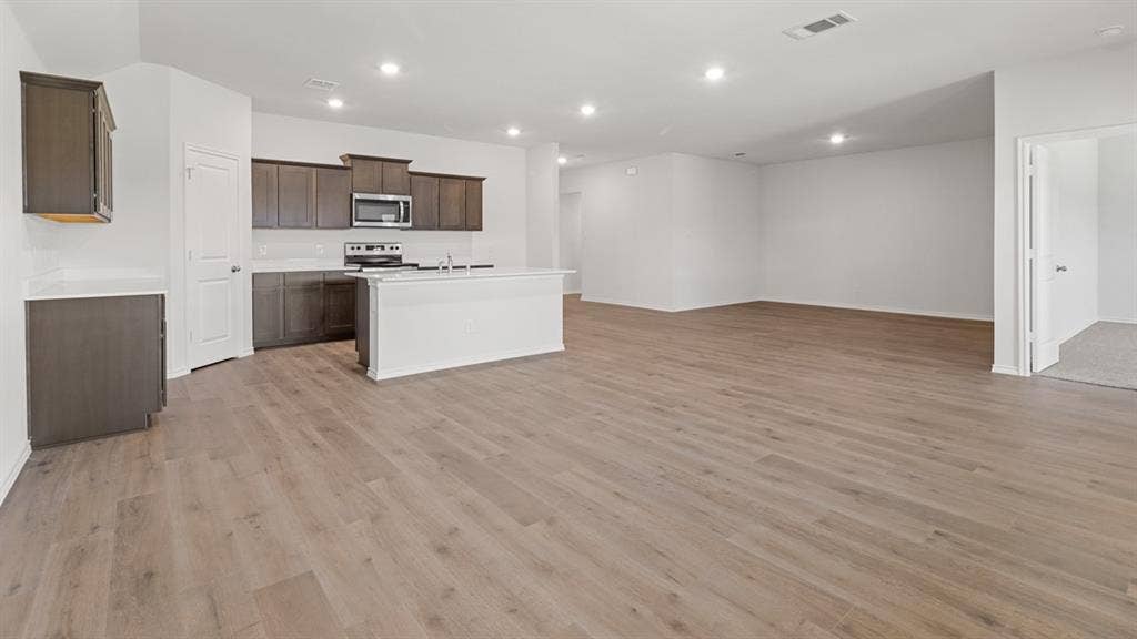 Open-concept living area featuring wood-finish flooring, a kitchen island, stainless steel microwave, and recessed lighting