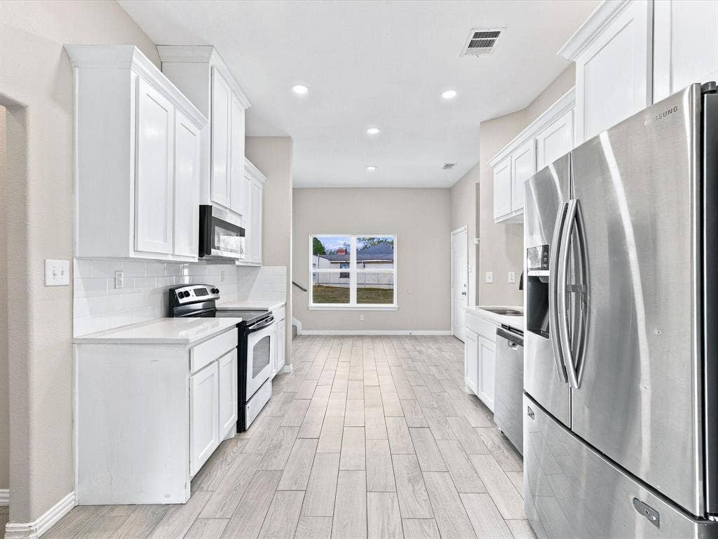 2312 Rogers Avenue, Lancaster, TX 75134 Kitchen featuring white cabinetry, solid-surface countertops, subway tile backsplash, stainless steel appliances, and wood-finish tile flooring