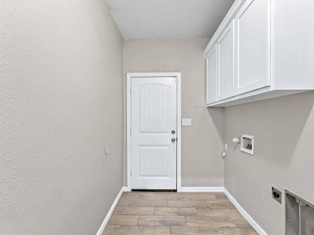 2312 Rogers Avenue, Lancaster, TX 75134 Utility area featuring wood-finish tile flooring, white shaker-style wall-mounted cabinetry, a solid-core entry door, and dedicated plumbing connections