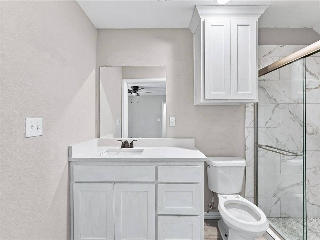 2312 Rogers Avenue, Lancaster, TX 75134 Bathroom featuring a white vanity cabinet with an integrated countertop, recessed mirror, wall-mounted upper cabinetry, and a walk-in shower with glass enclosure