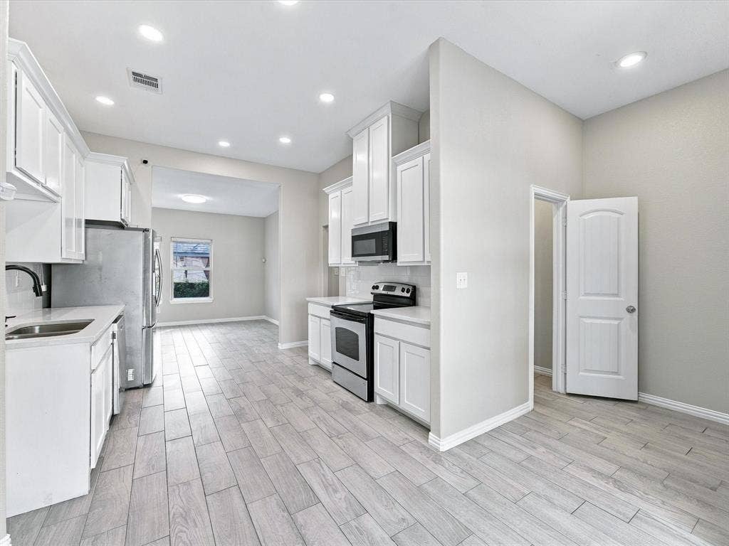 2312 Rogers Avenue, Lancaster, TX 75134 Kitchen featuring white shaker-style cabinetry, stainless steel appliances, wood-finish tile flooring, recessed lighting, and solid-surface countertops
