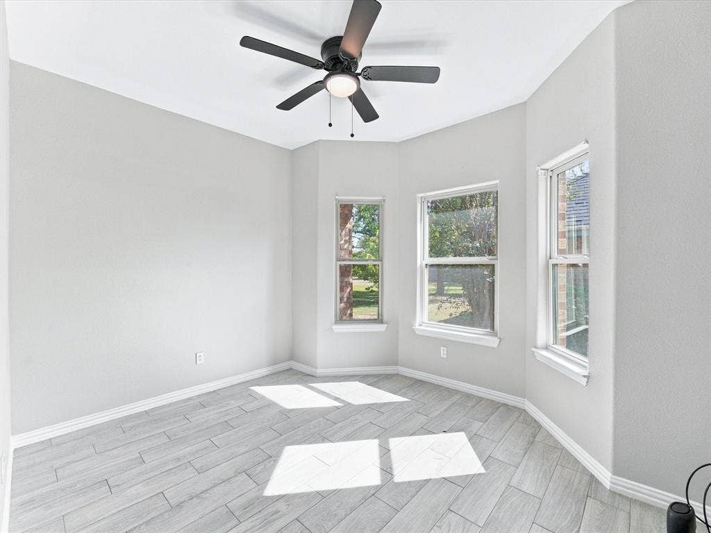 2312 Rogers Avenue, Lancaster, TX 75134 Interior space featuring neutral-toned walls, wood-finish tile flooring, three large windows, and a ceiling-mounted light fixture with a fan