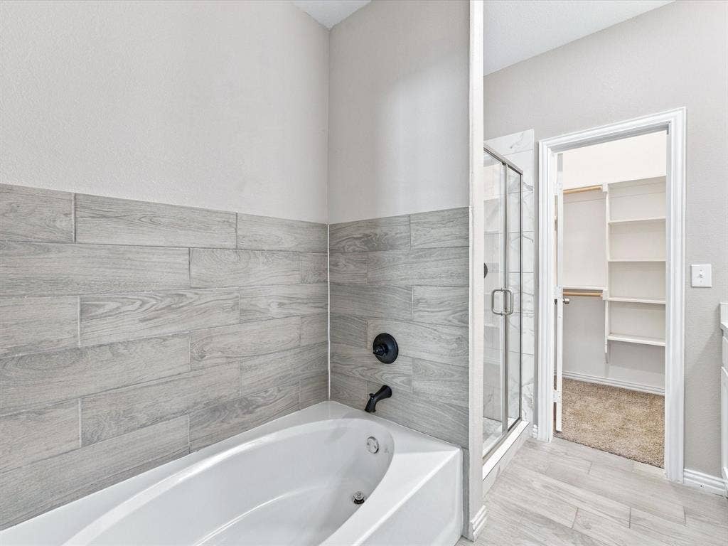 2312 Rogers Avenue, Lancaster, TX 75134 Soaking tub featuring wood-finish tile surround, separate glass-enclosed shower, matte black plumbing fixtures, and walk-in closet with built-in shelving