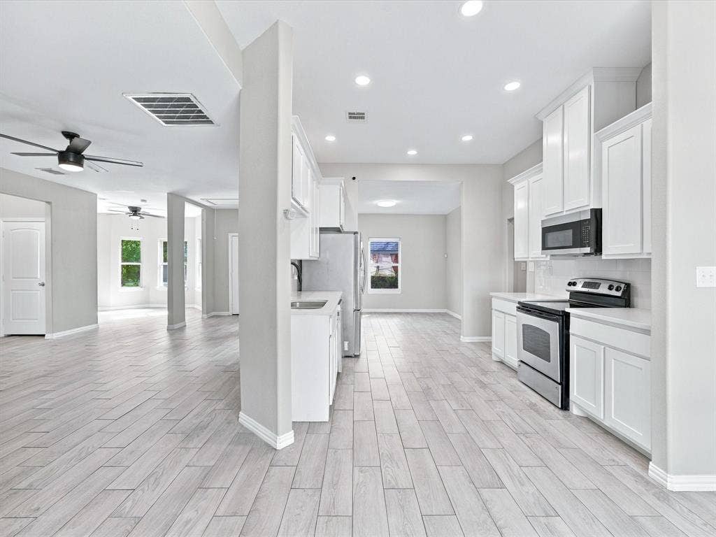 2312 Rogers Avenue, Lancaster, TX 75134 Kitchen featuring white cabinetry, stainless steel appliances, and solid surface countertops, complemented by recessed lighting and light-toned wood-finish flooring