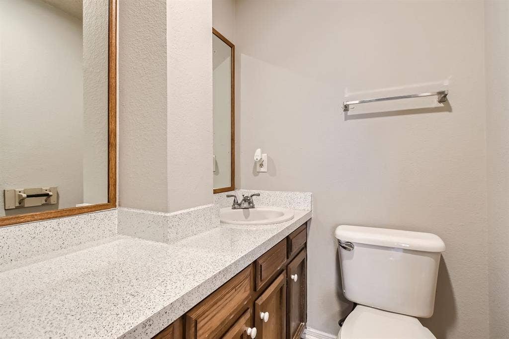 806 Prairie Creek Drive, Princeton, TX 75407 Bathroom vanity featuring a speckled composite countertop, undermount sink with dual-handle faucet, wood cabinetry, and framed wall mirror