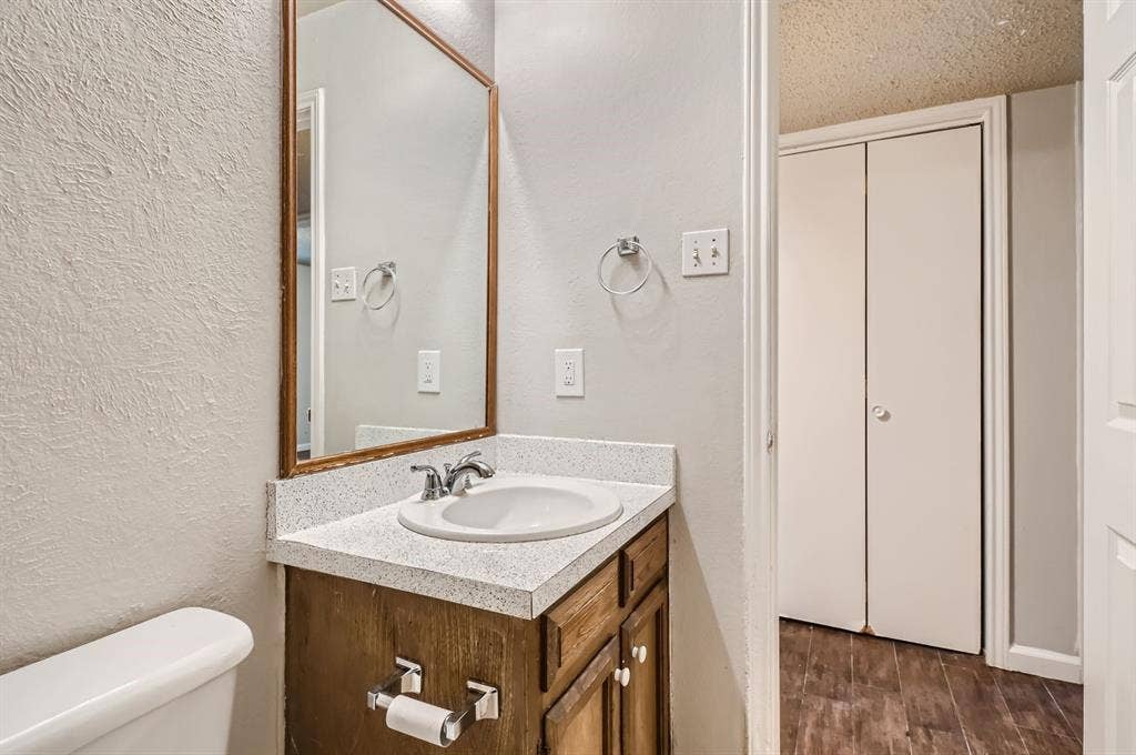 806 Prairie Creek Drive, Princeton, TX 75407 Wood-finish cabinetry featuring a light-toned solid surface countertop, integrated sink with polished chrome hardware, framed mirror, and double-door closet