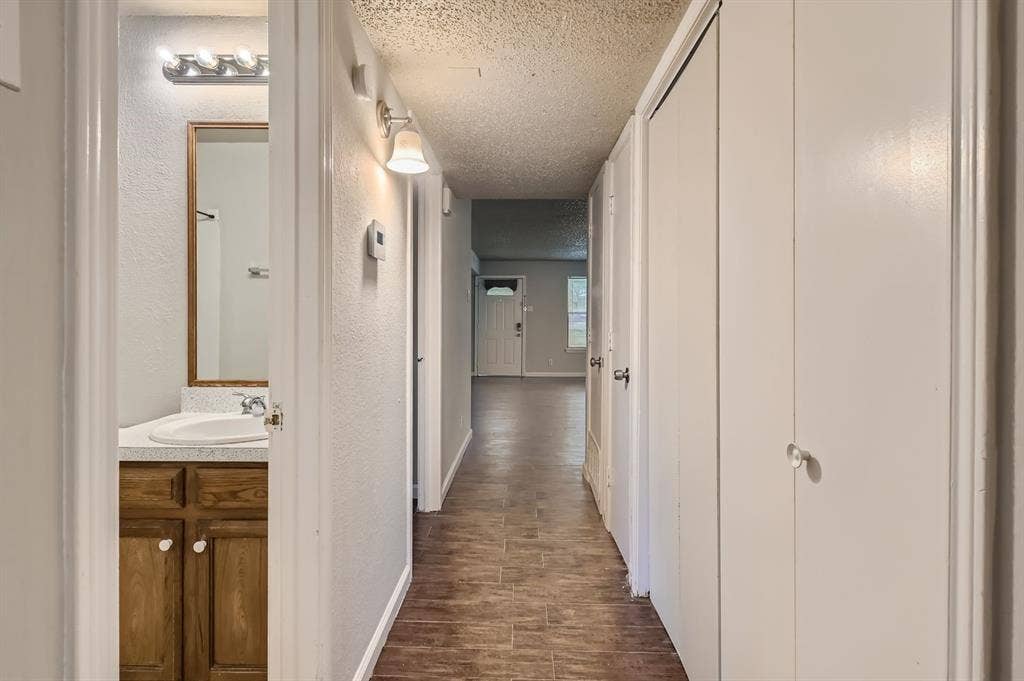 806 Prairie Creek Drive, Princeton, TX 75407 Hallway featuring wood-finish flooring, white bifold closet doors, and a bathroom containing a vanity with a stone-surface countertop, integrated basin, and wood-finish cabinetry