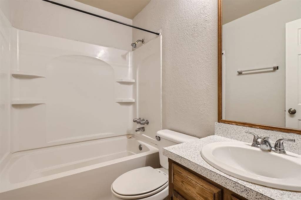 806 Prairie Creek Drive, Princeton, TX 75407 Bathroom featuring a molded composite tub and shower surround with integrated shelving, vanity with a speckled composite countertop, undermount sink, and wood-finish cabinetry