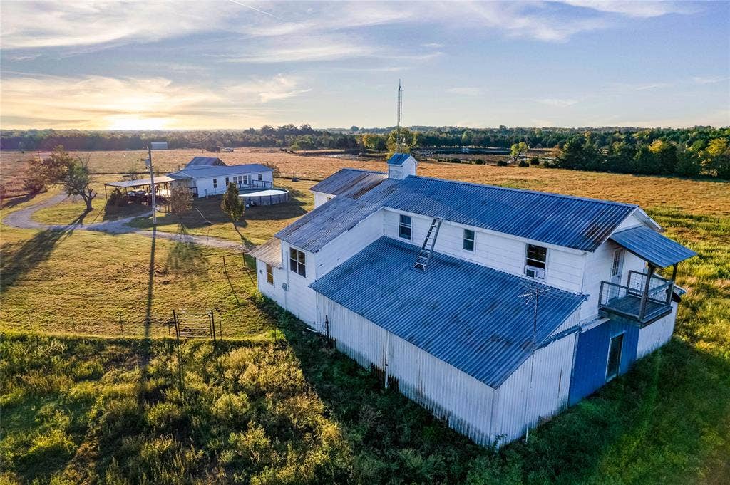 1154 Outlaw Trail, Wolfe City, TX 75496 Expansive rural acreage featuring a two-story outbuilding with a metal roof, an elevated wooden balcony, and an additional secondary structure situated on the grounds