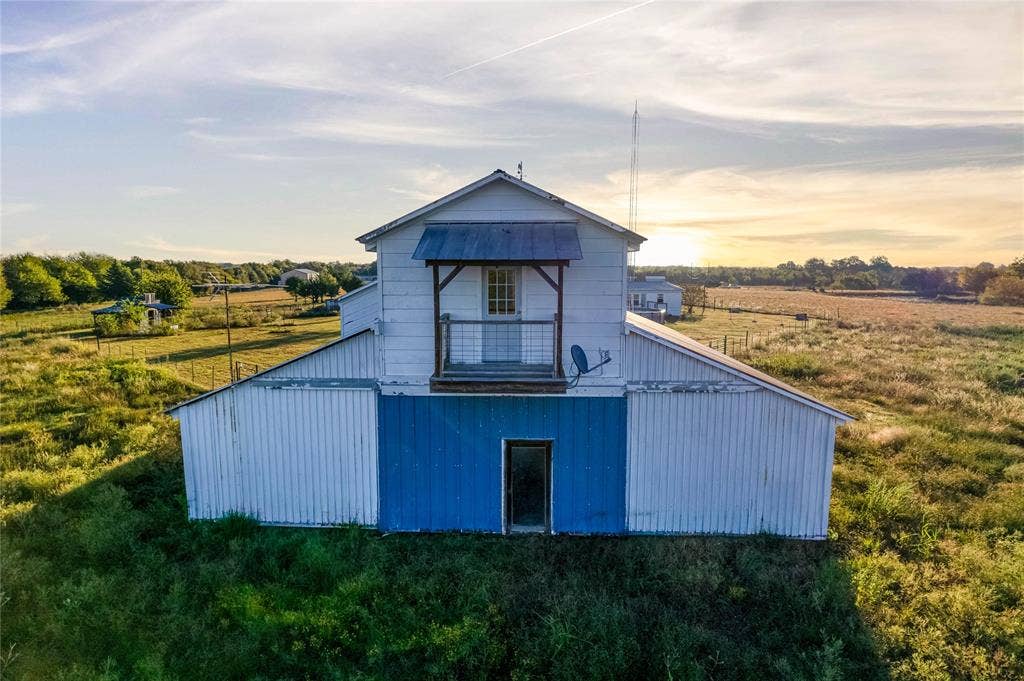 1154 Outlaw Trail, Wolfe City, TX 75496 Two-story structure with corrugated metal siding, upper-level balcony with metal railing, and metal gable roof