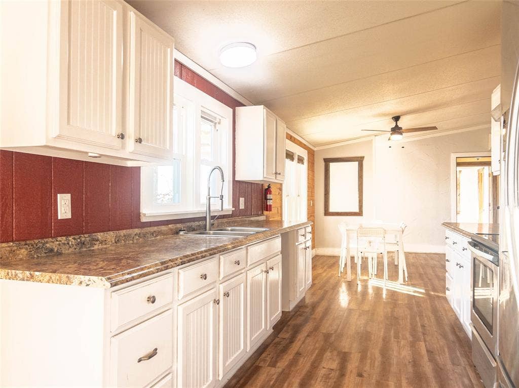 1154 Outlaw Trail, Wolfe City, TX 75496 Kitchen featuring white cabinetry, stone-finish countertops, stainless steel sink with high-arc faucet, and wood-finish flooring